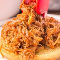 Tongs placing some shredded BBQ chicken on a bun.