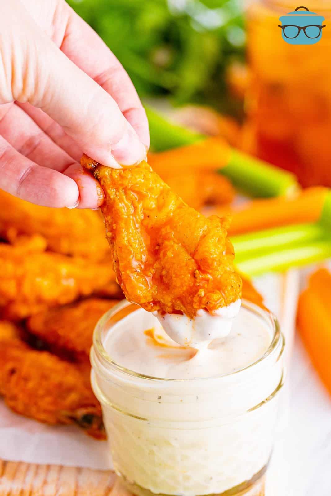 A hand dipping a crispy chicken wing in sauce.