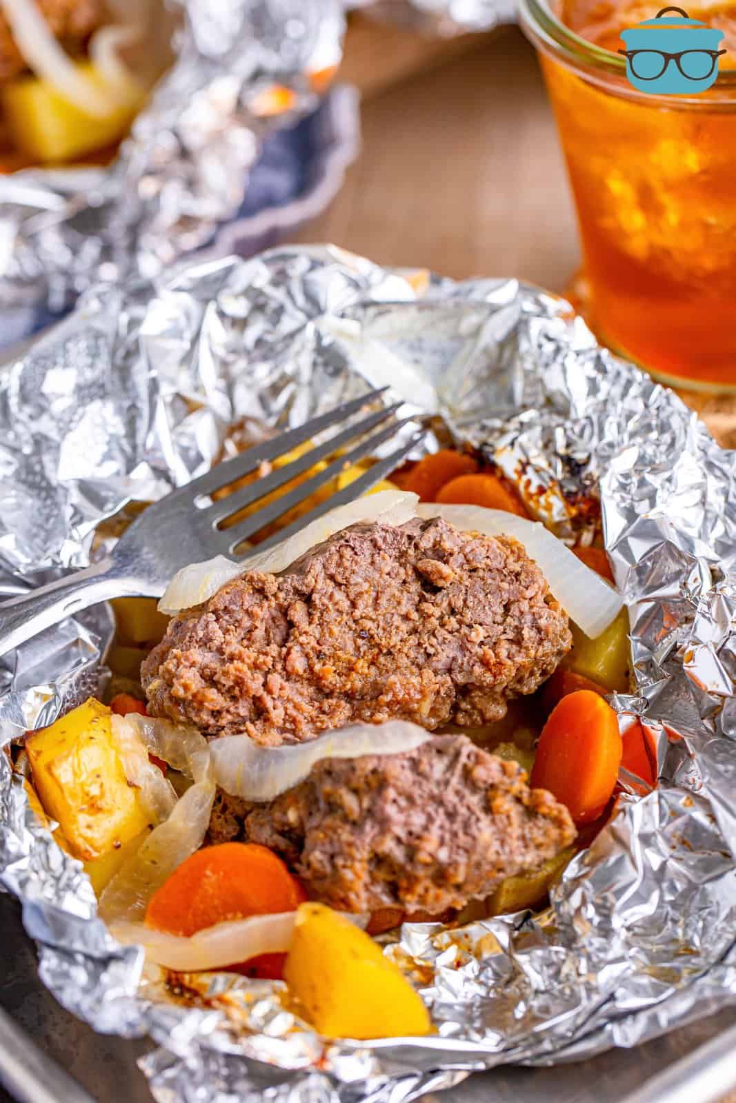 Aluminum foil packet with a burger patty, potatoes and carrots.