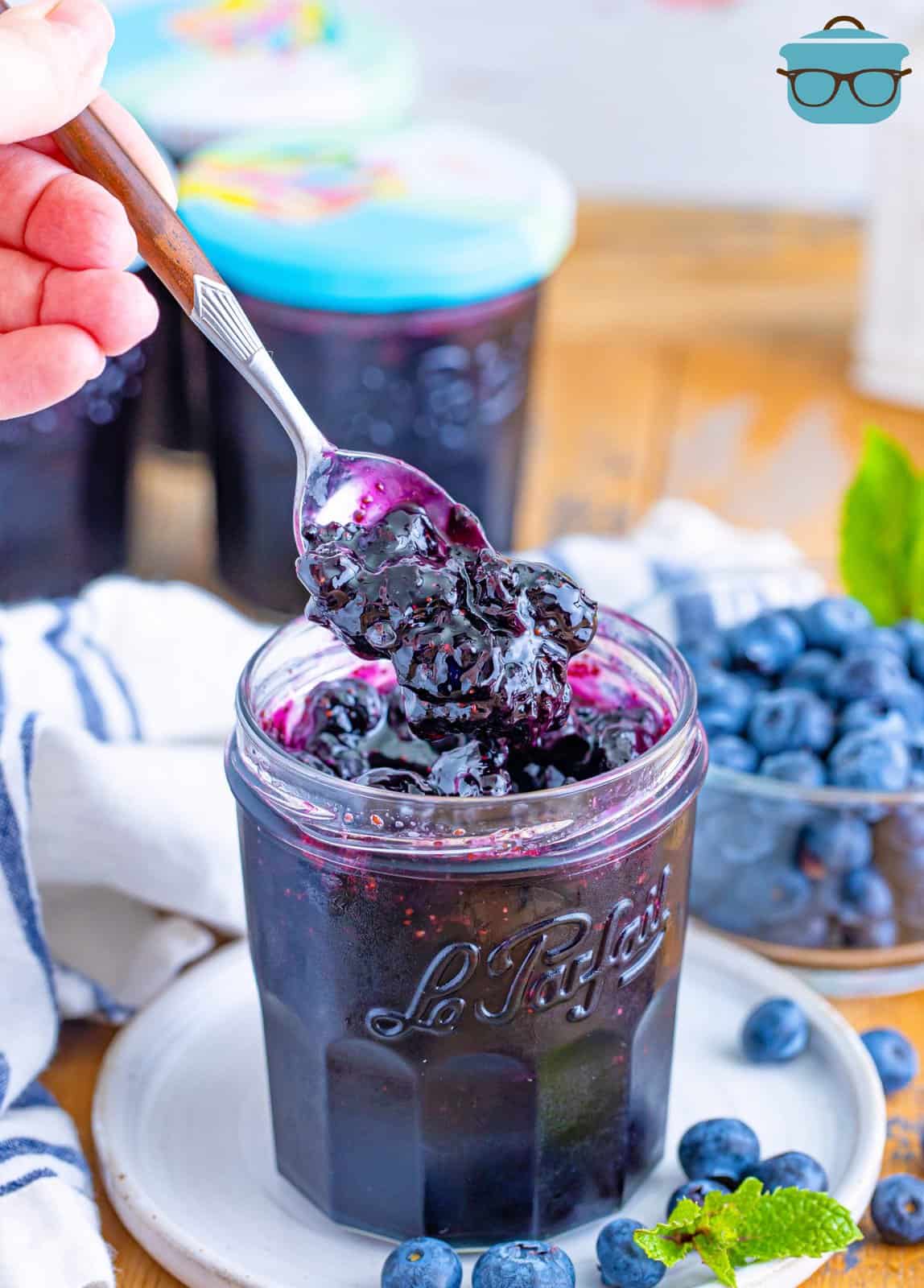A spoon holding some blueberry jam over the jar of it.