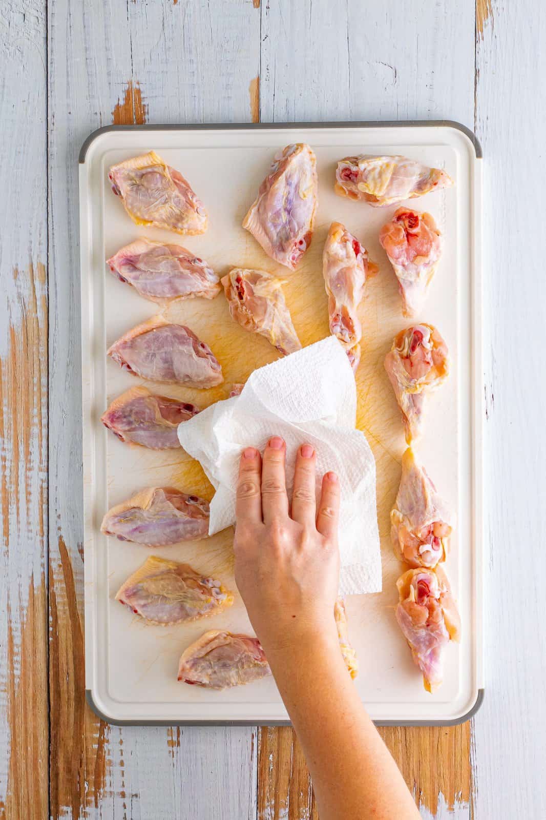 A hand patting chicken wings with paper towels.