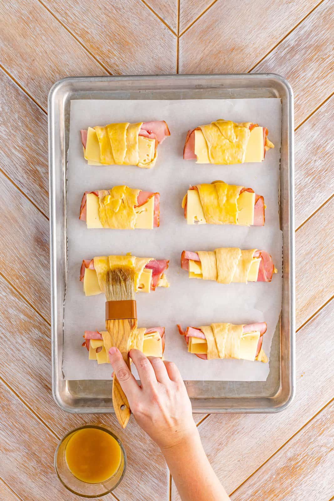 A hand brushing the butter on the stuffed ham and cheese rolls.