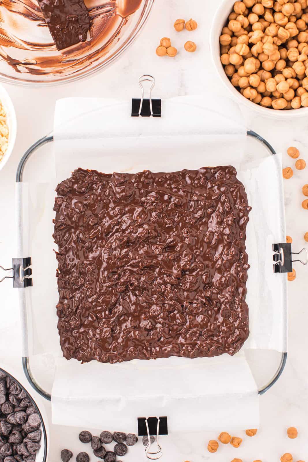 A baking dish lined with parchment paper, with melted chocolate and Rice Krispies.
