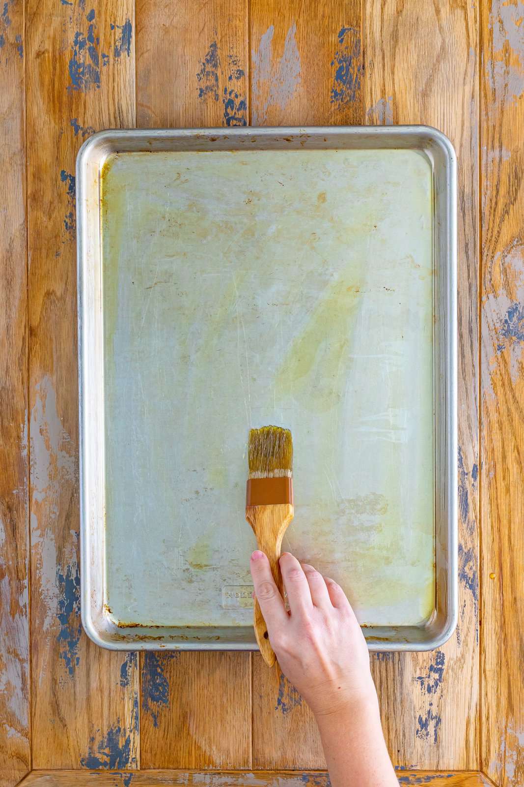 A sheet pan being brushed with oil.