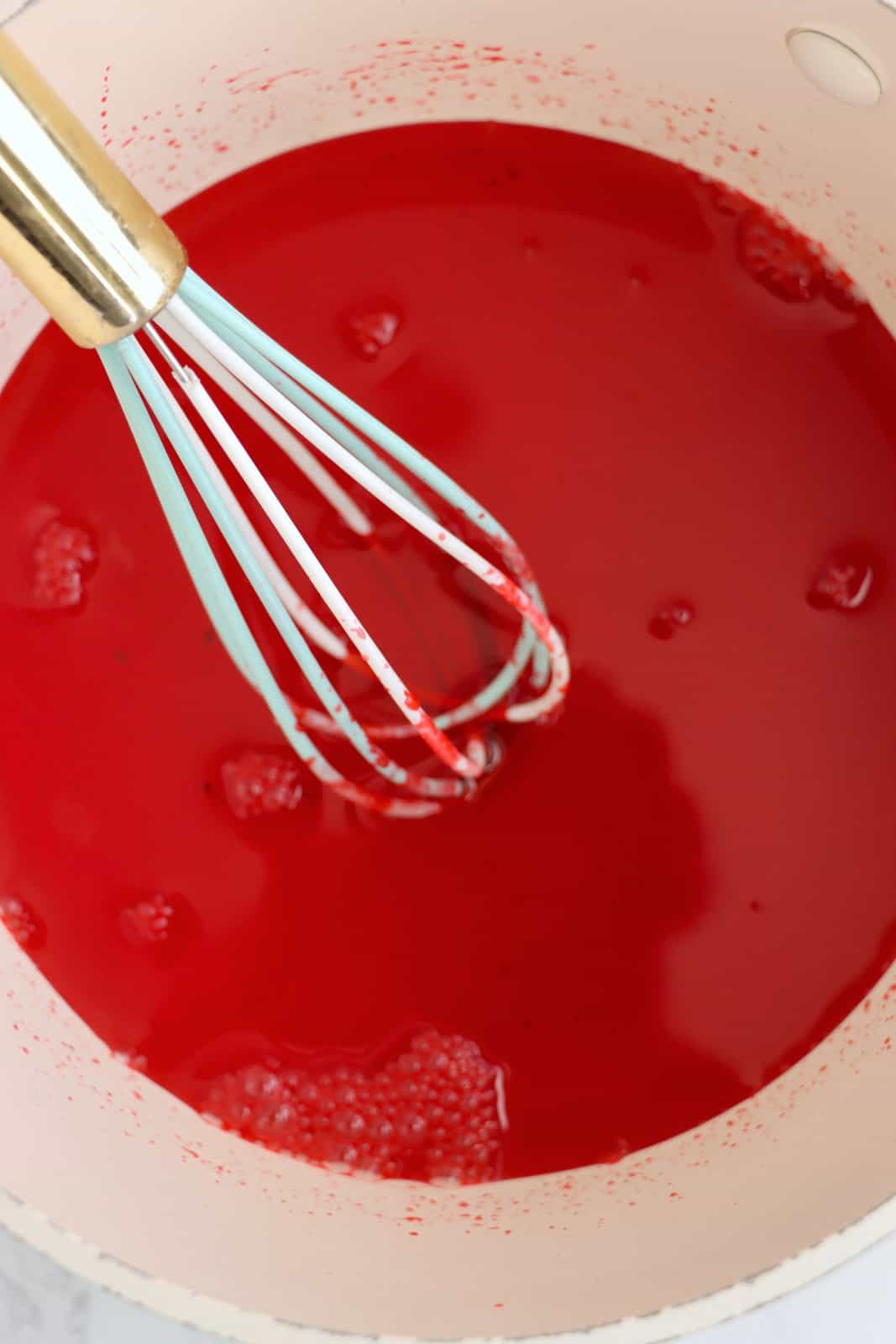 Cherry jello mixture in a bowl with a whisk,