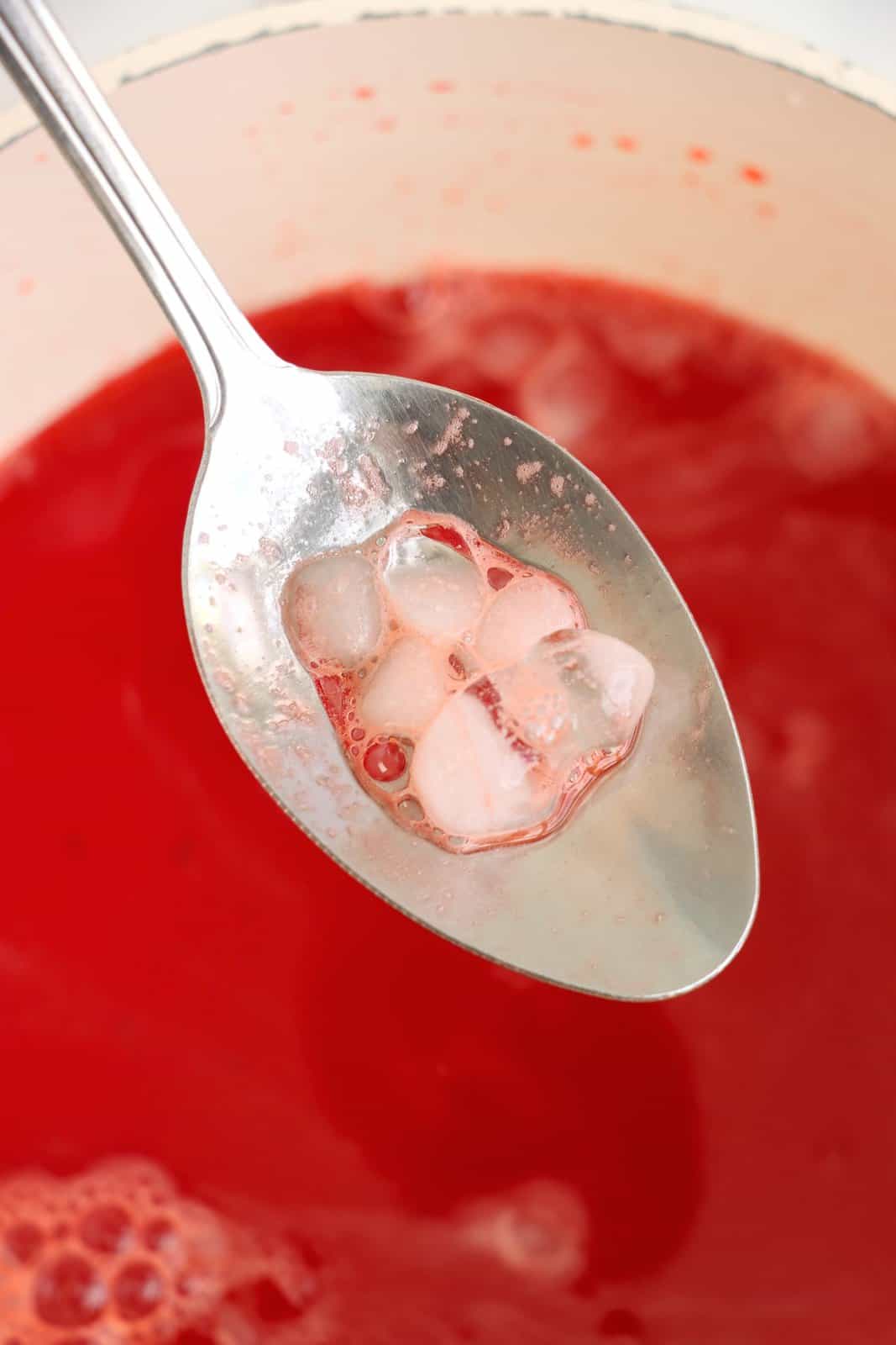 A spoon removing ice from a bowl of liquid gelatin.