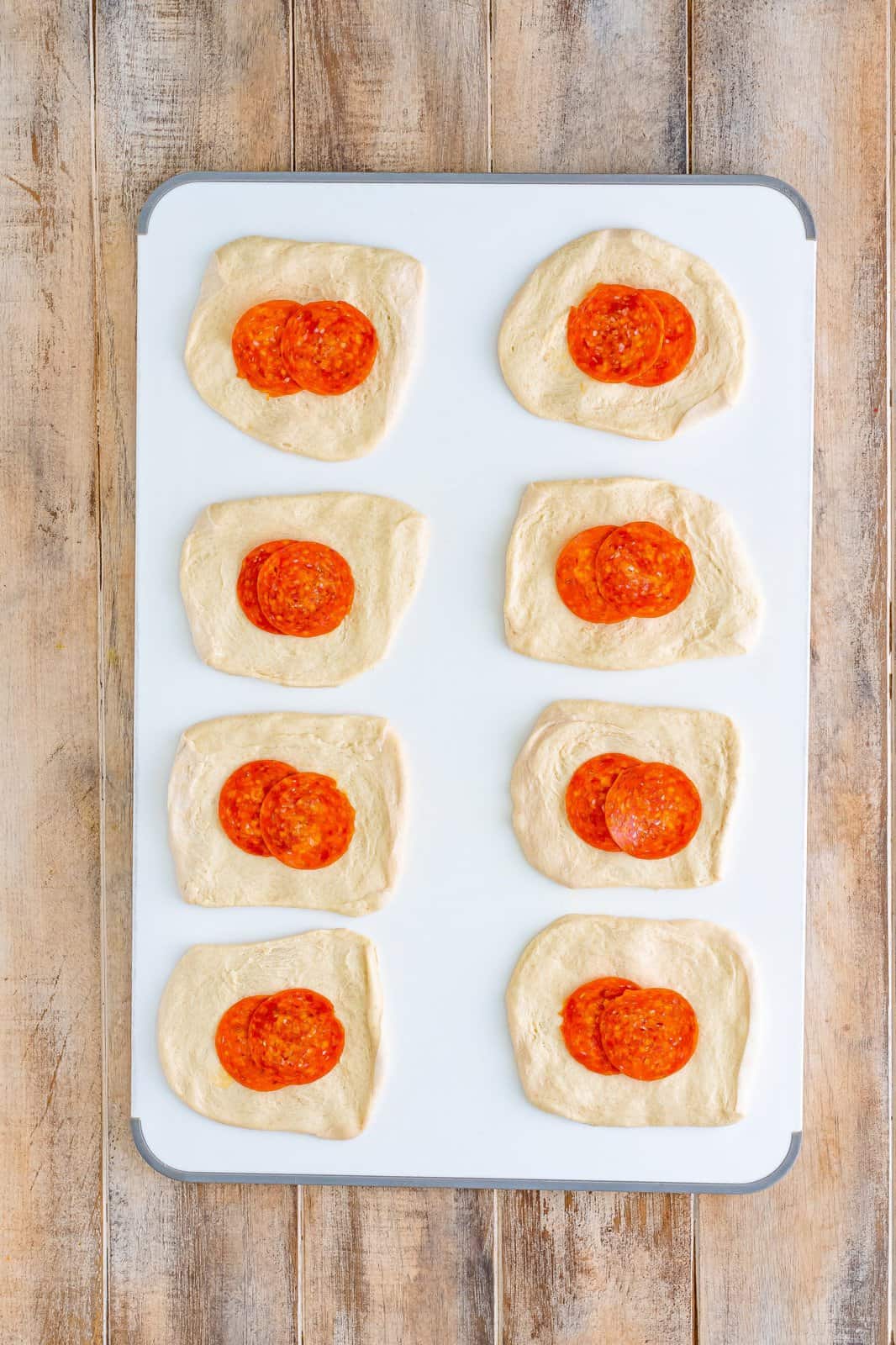 Flattened bread dough with pepperoni slices.