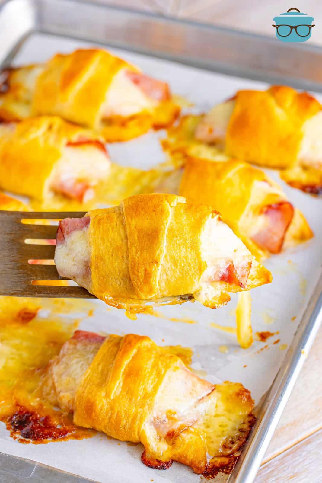 A serving utensil holding up a Ham and Cheese Crescent Roll above a plate.