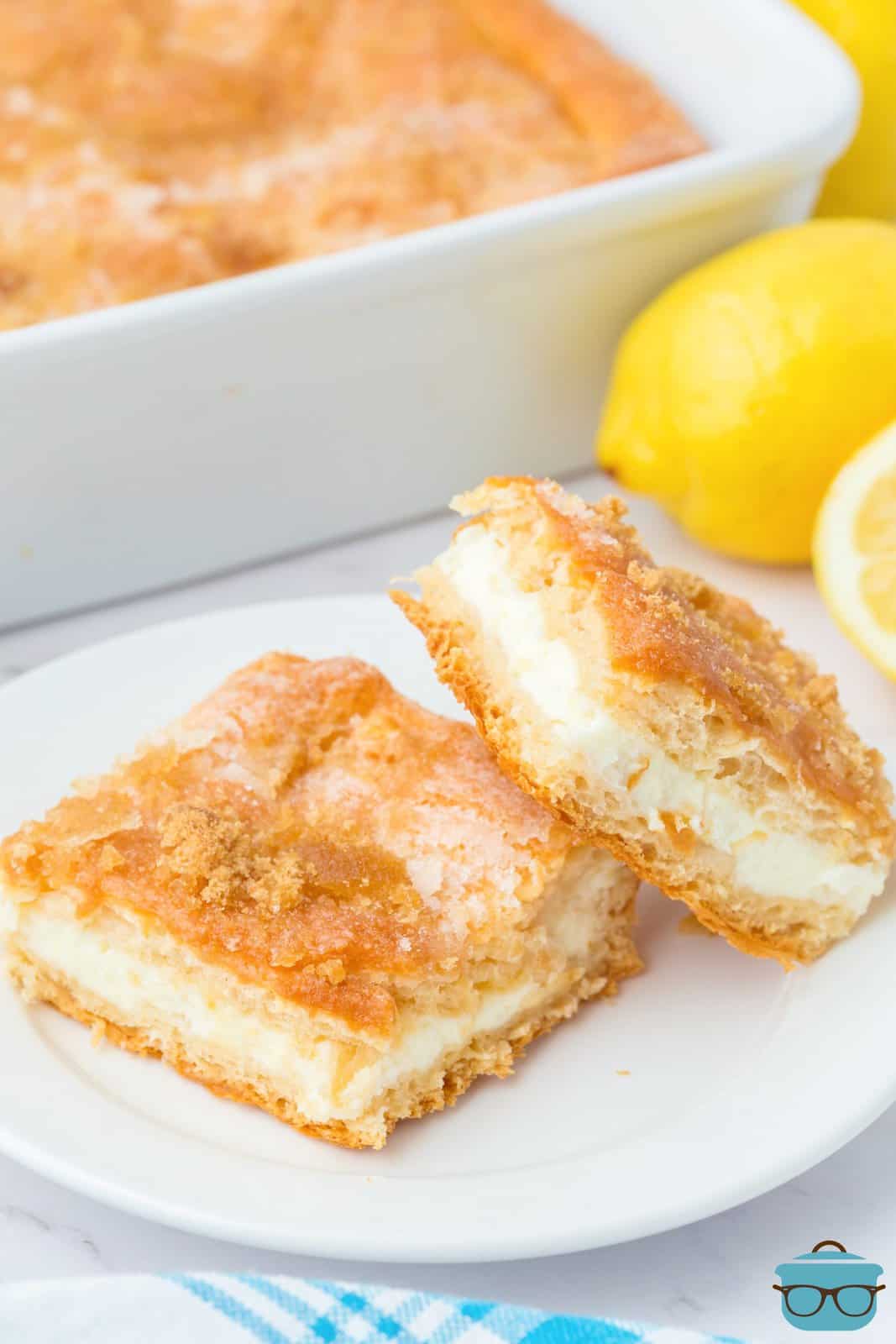 A plate with two lemon cheesecake bars, one on an angle.