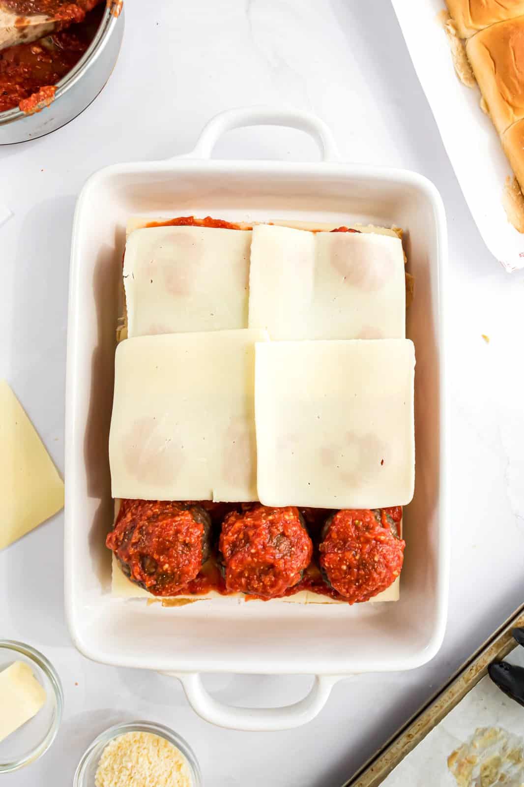 Meatballs on buns with sauce, and more cheese. 