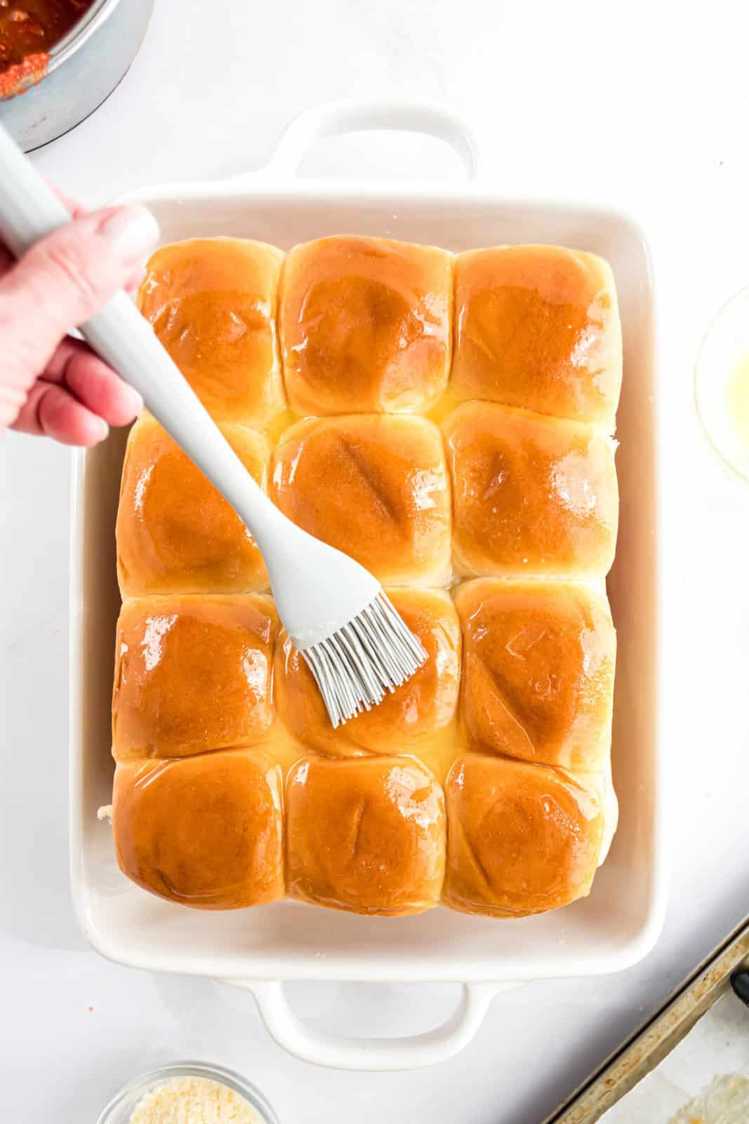 Melted butter being brushed on top of slider buns.