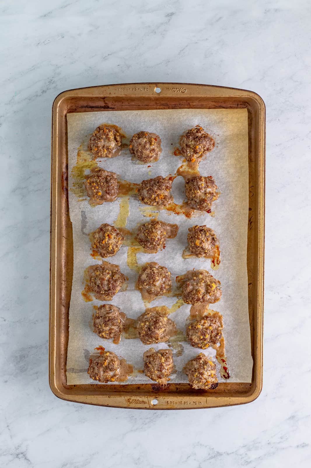 fully cooked meatballs on a parchment paper lined baking sheet. 