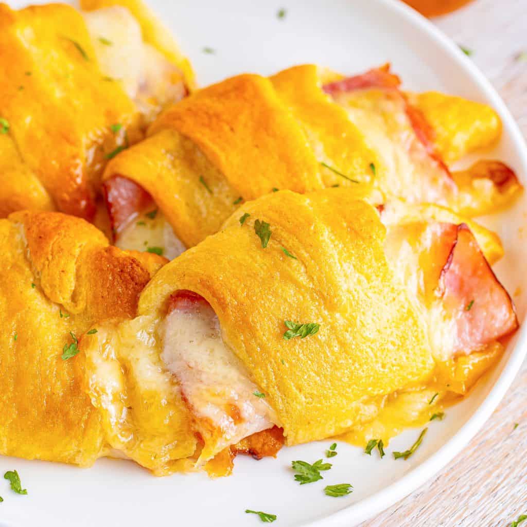 Closely looking at a Ham and Cheese Crescent Roll with the ham and gooey cheese exposed on the ends.