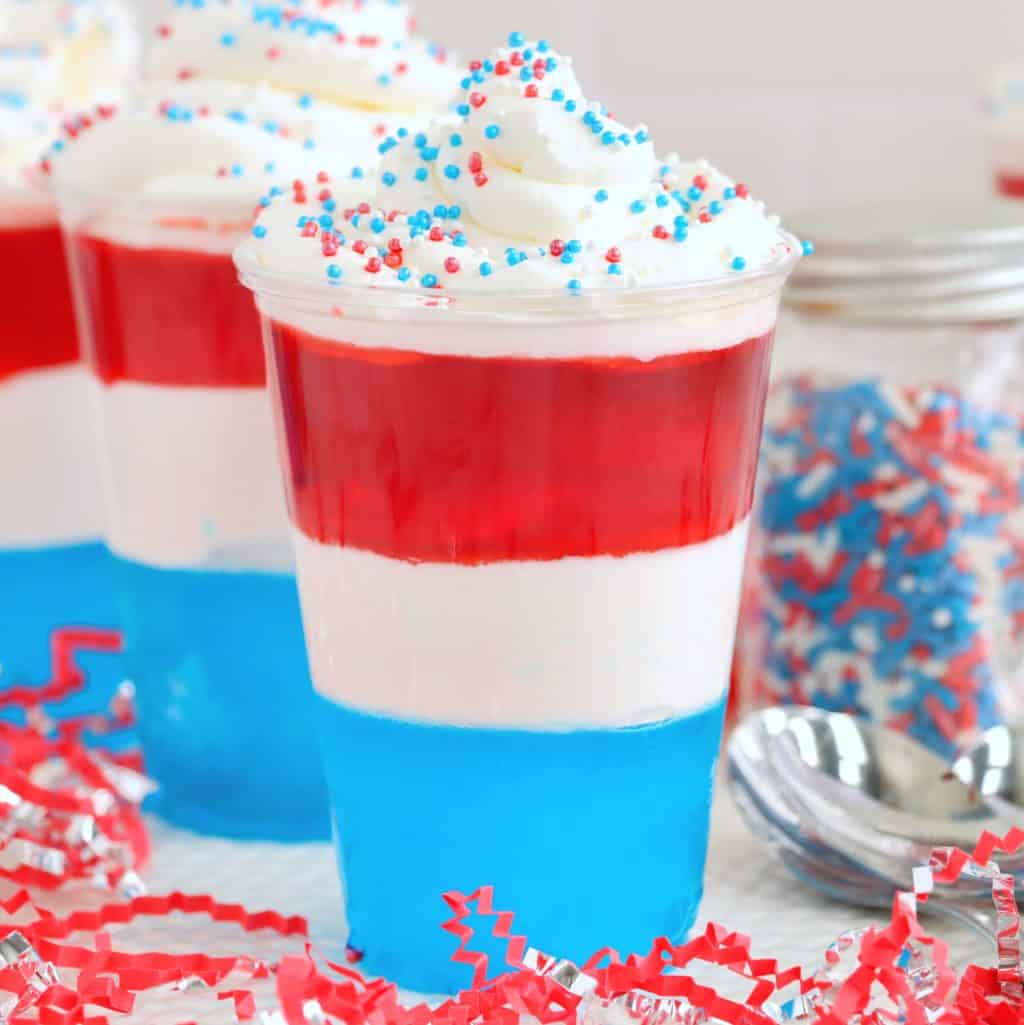 A few layered Red, white, and blue jello cups with whipped cream and sprinkles.