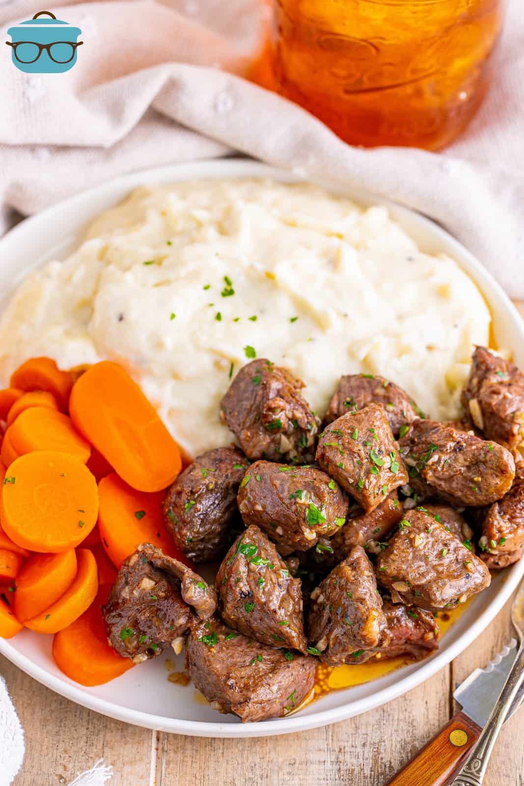 A plate with mashed potatoes, Air Fryer Garlic Butter Steak Bites and carrot pieces. 