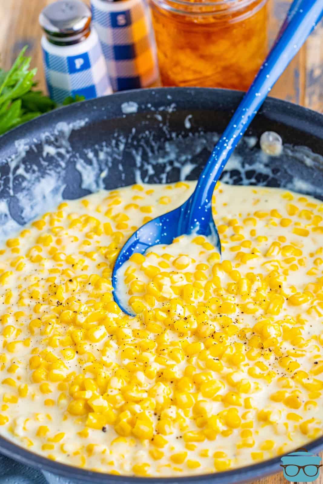A skillet with creamed corn and a blue serving spoon.