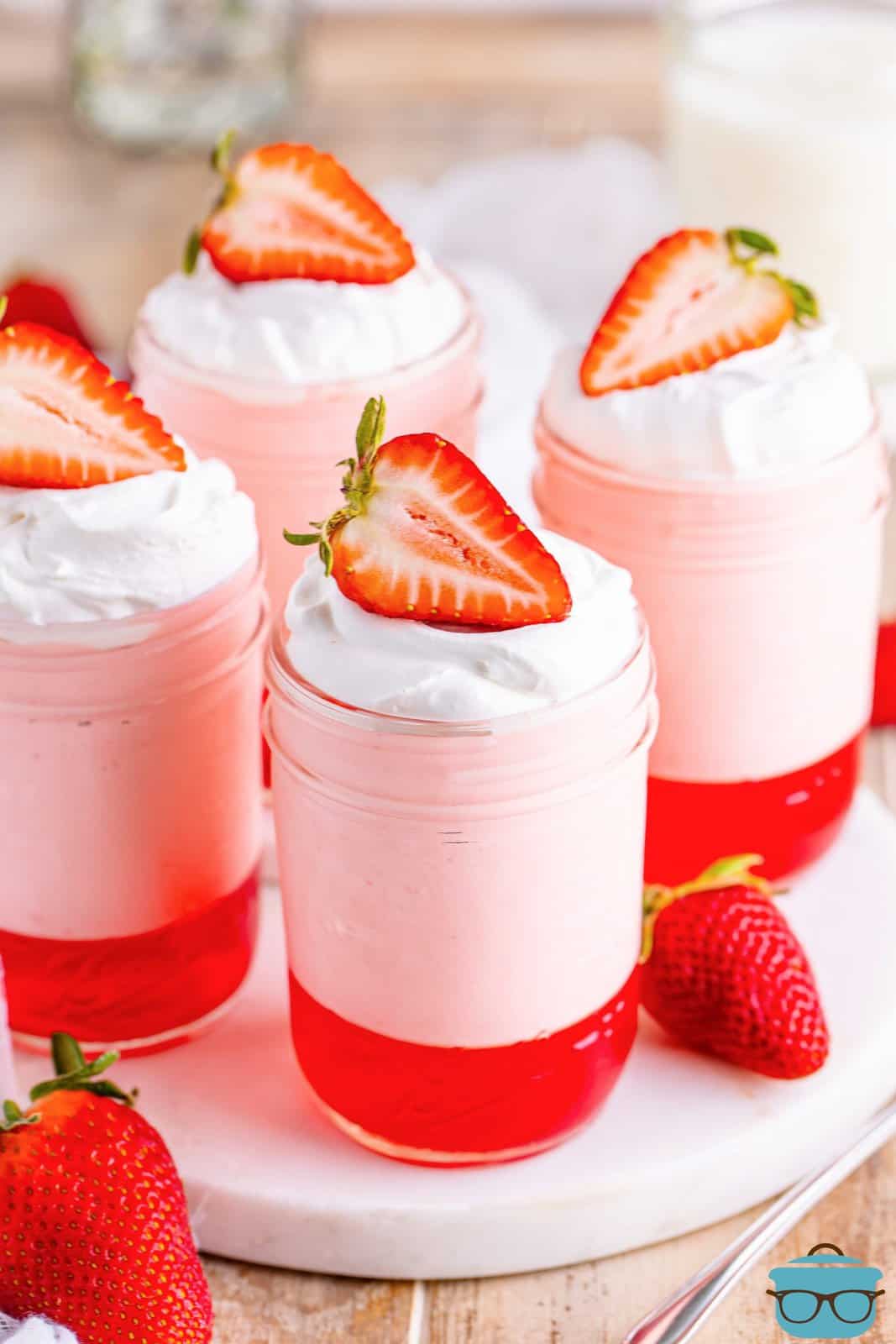 Four jars of strawberry Jell-O parfait with strawberries on top.