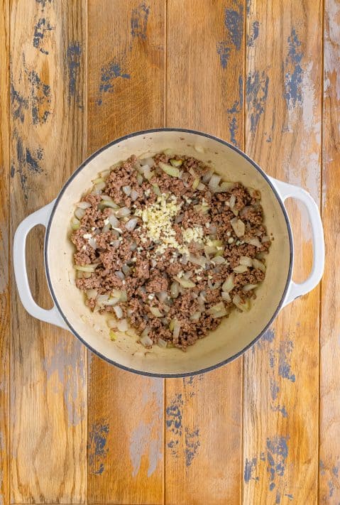 Garlic, ground beef, onion, and bacon in a skillet.