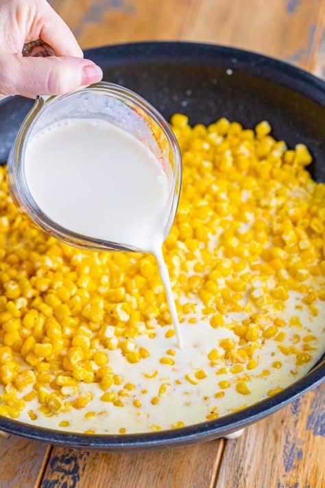 Milk being added to a skillet with corn.