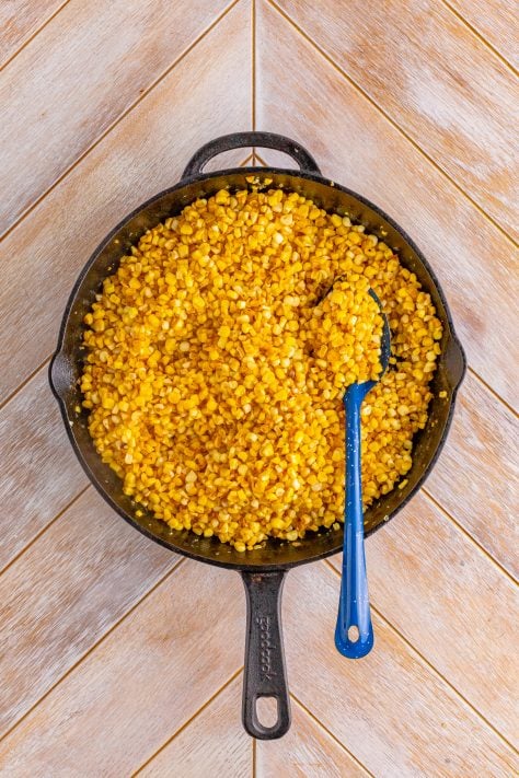 A spoon in a cast iron skillet of fried corn.