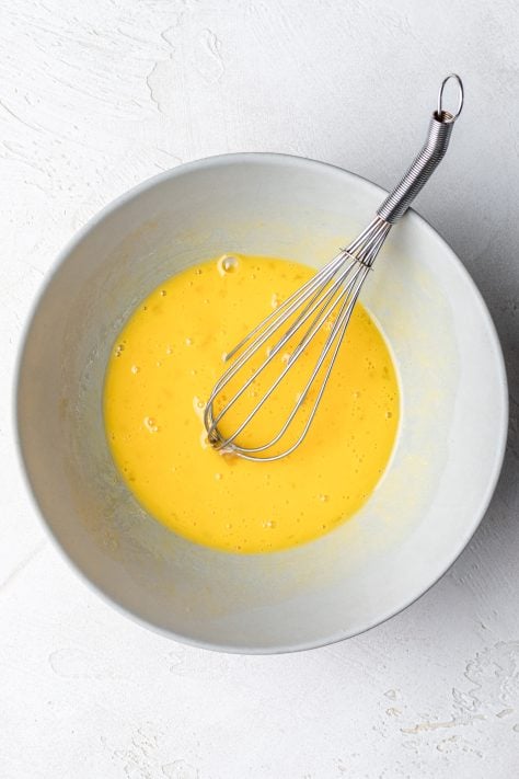 A mixing bowl with whisk, eggs, egg yolks and water.