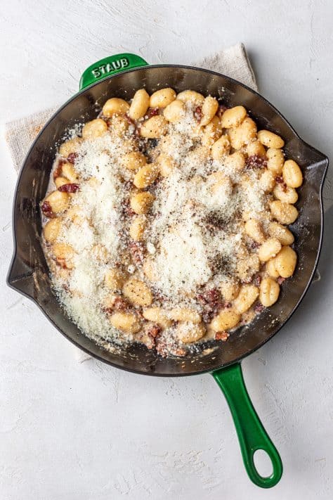 Grated cheese over gnocchi and bacon.