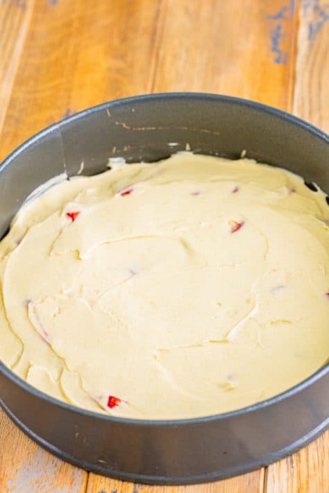 Cake batter on top of strawberry mixture in a springform pan.