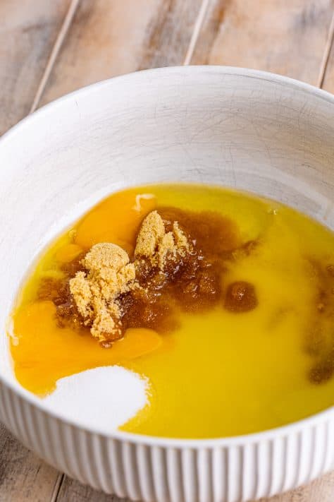 A mixing bowl with egg, egg yolk, oil, butter, brown sugar, granulated sugar, and vanilla.