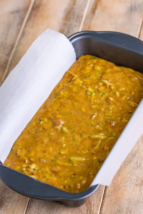 A parchment lined loaf pan with zucchini bread batter.