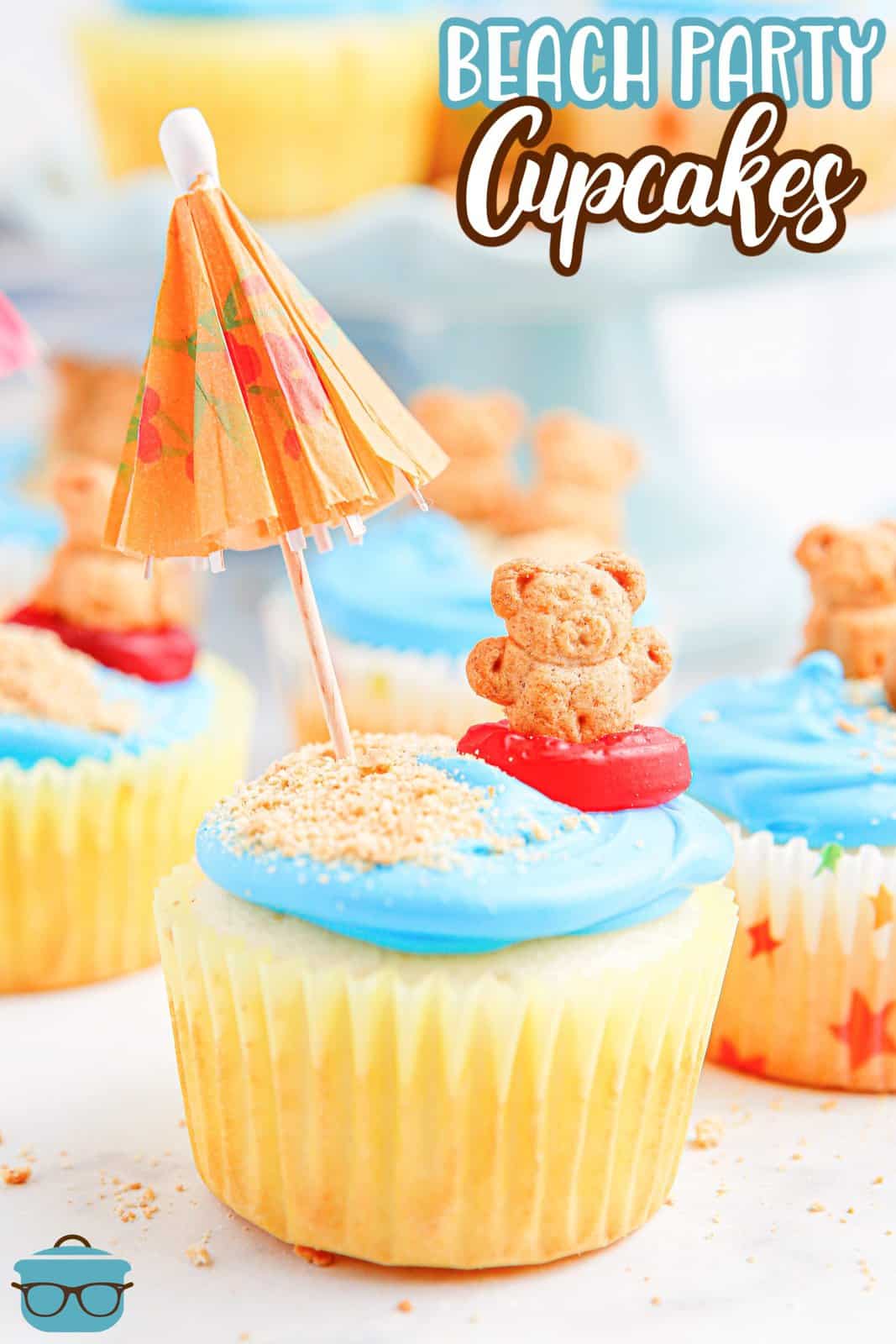 a closeup of a cupcake with blue frosting and a teddy graham bear and a small cocktail umbrella. 