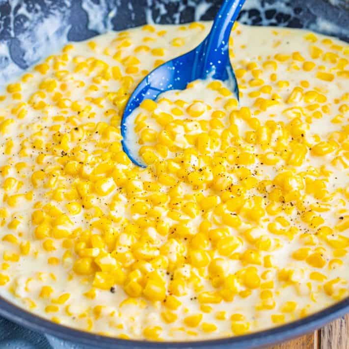 A blue serving spoon in a skillet of creamed corn.