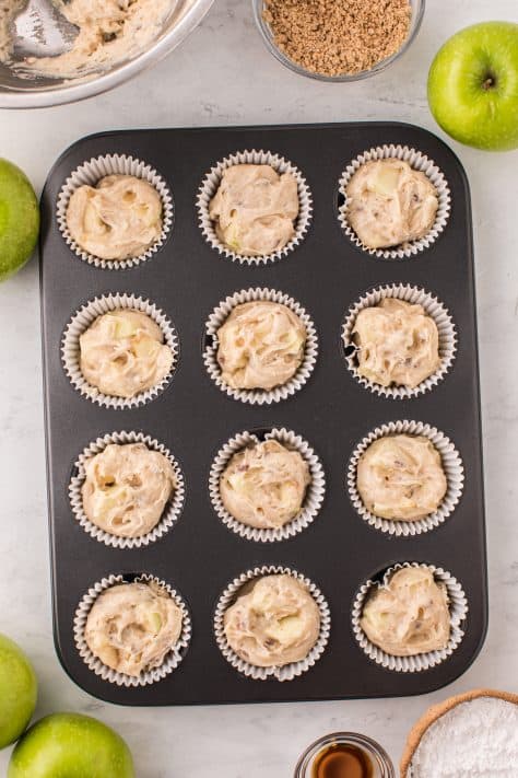Lined muffin mix tin with muffin batter in each well.