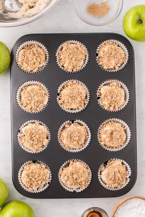 Muffin batter in a lined muffin tin with streusel topping on top.
