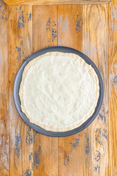 Pizza dough and white sauce on a pizza pan.
