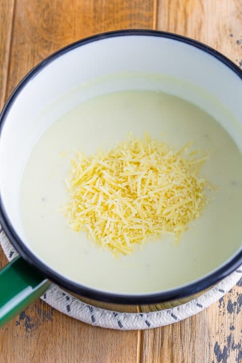 A white sauce with shredded cheese on top in a sauce pan.