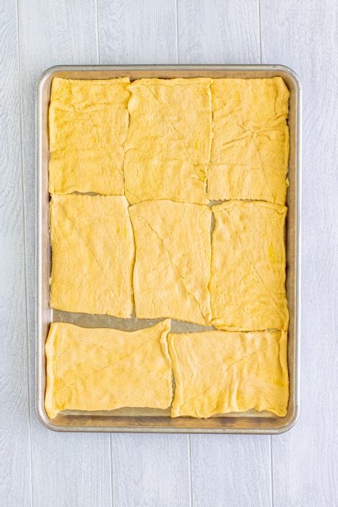 A baking sheet with crescent roll dough pinched together.