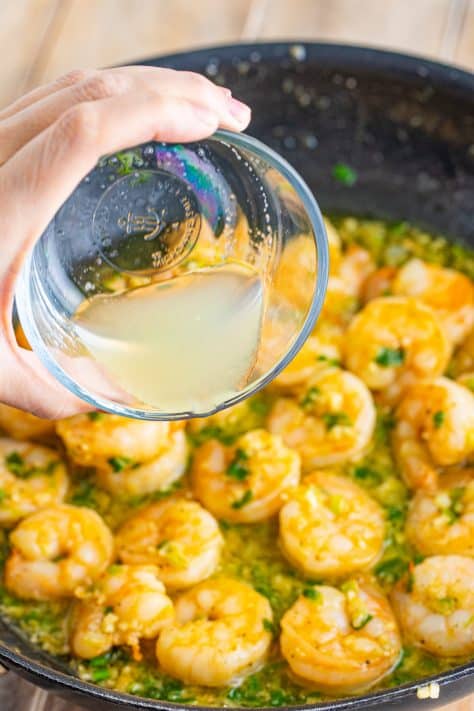 Lemon juice being poured into a pan of cooked shrimp.