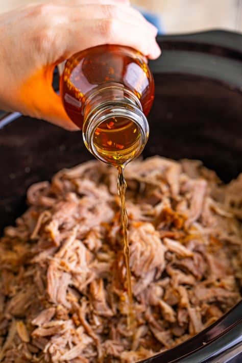 Sauce being drizzled on top of Pulled Pork in a crock pot.