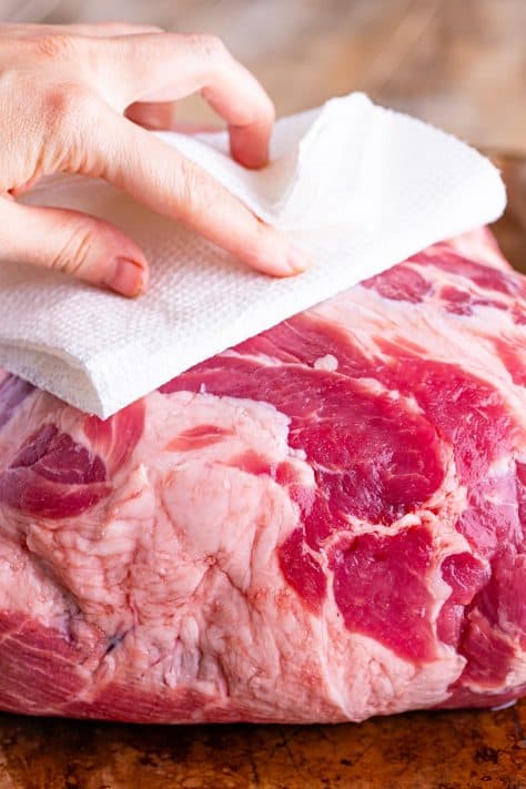 A pork roast being patted dry by a paper towel.