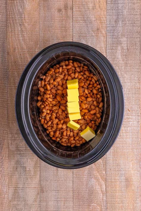 Drained and cooked beans with butter on top in a slow cooker.