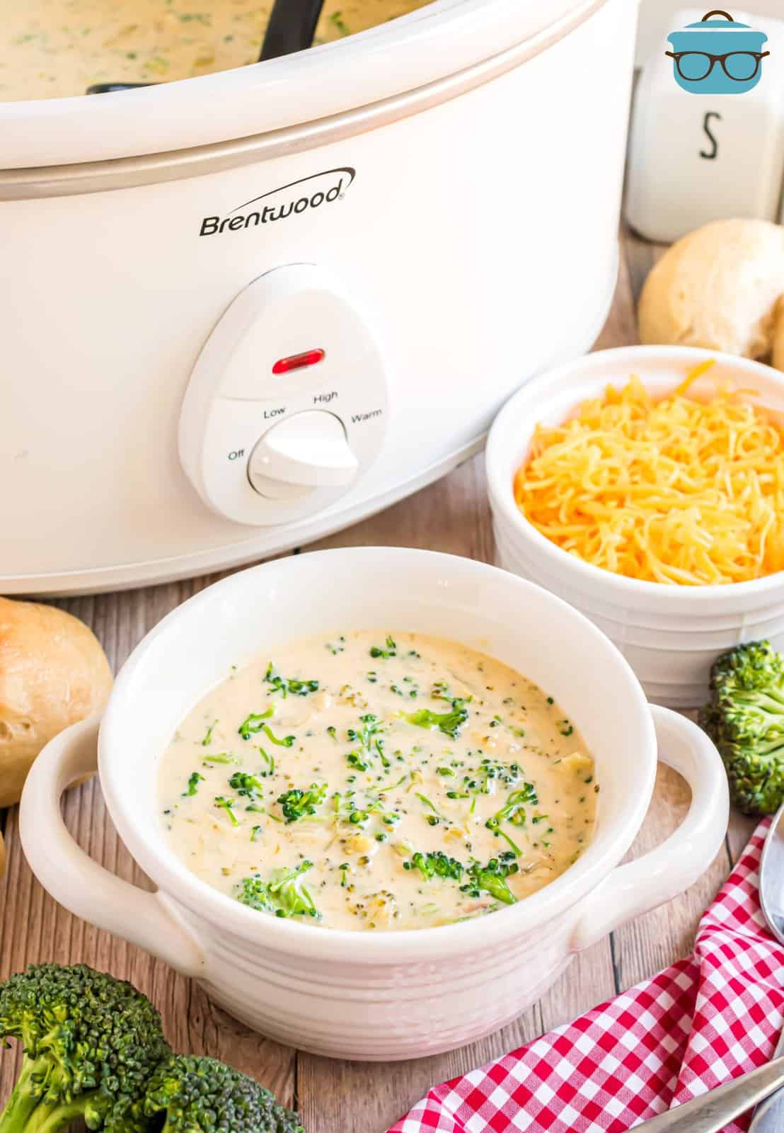 A bowl of broccoli cheddar soup sitting in front of a Crock pot.