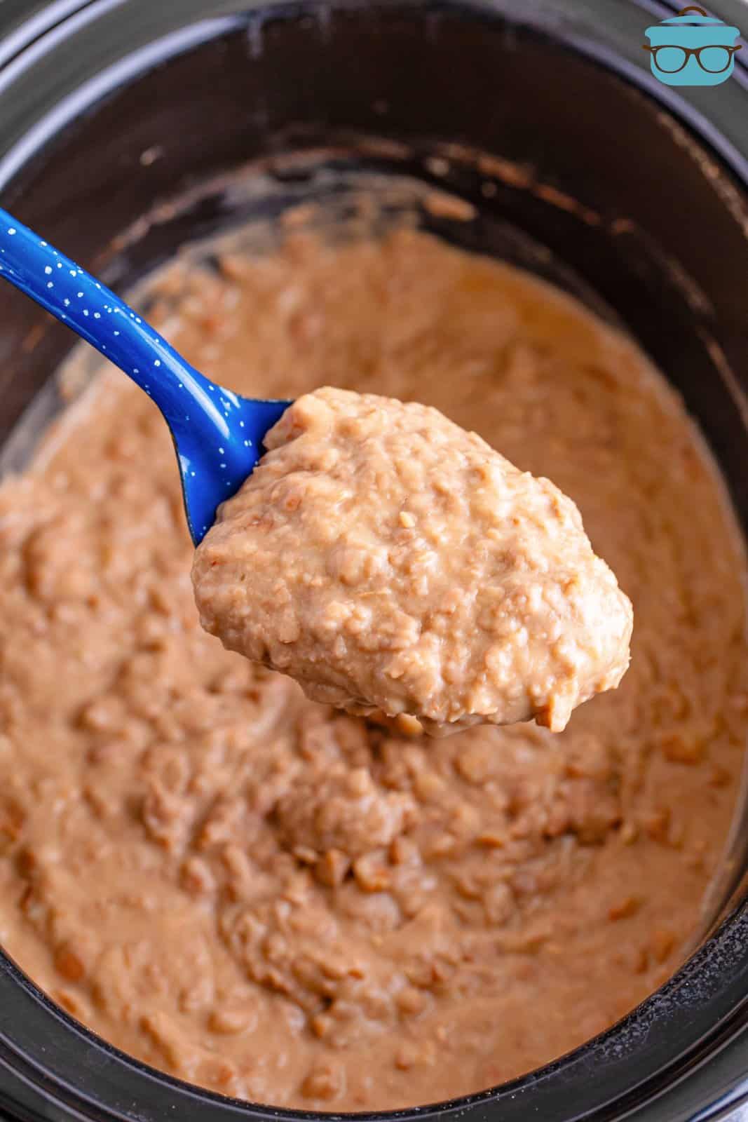 A serving spoon of refried beans above the Slow Cooker.