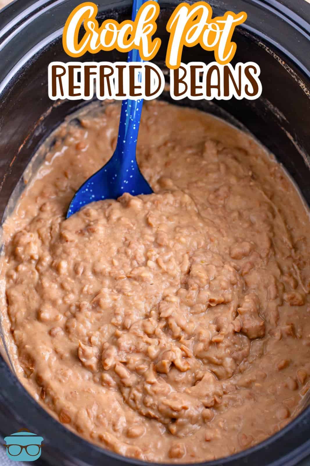 A blue serving spoon in a slow cooker of refried beans.
