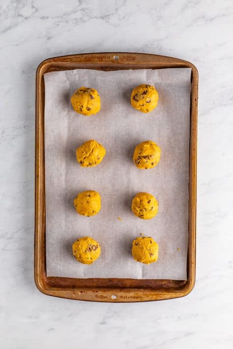 Rolled cookie dough balls on a parchment lined baking sheet.