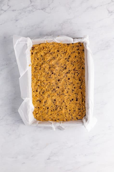 A baking pan with parchment paper and cookie dough pressed out.
