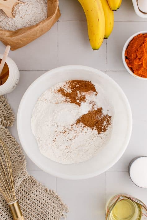 A mixing bowl with all-purpose flour, pumpkin pie spice, ground cinnamon, baking powder, baking soda and salt.