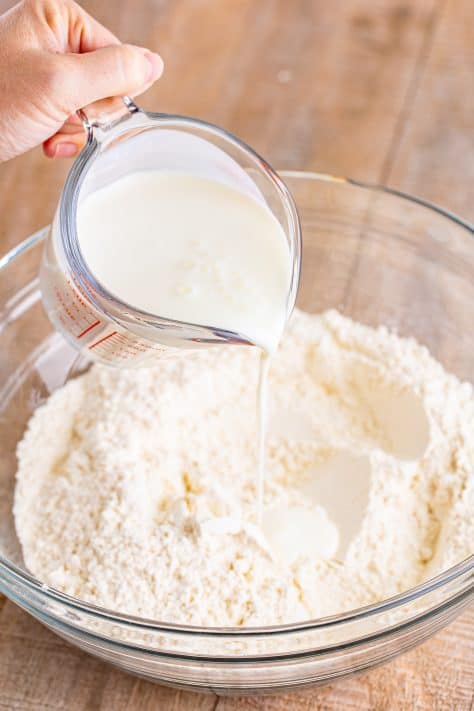Buttermilk being poured in the dry ingredients in a mixing bowl.