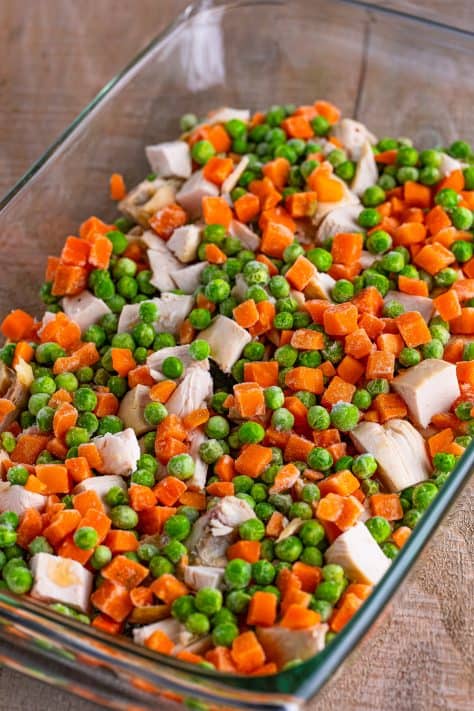 Melted butter, rotisserie chicken and frozen peas and carrots in a baking dish.