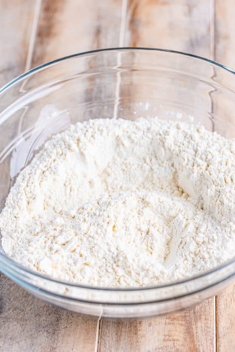 A glass mixing bowl with all-purpose flour, granulated sugar, aluminum-free baking powder, salt and garlic powder.