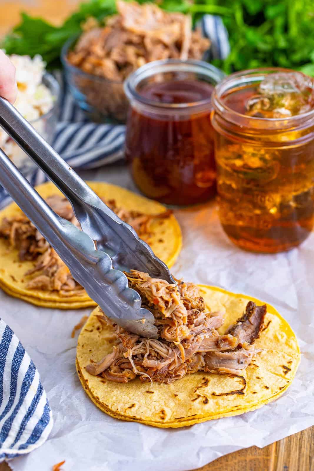 Shredded bbq pork being placed on top of corn tortillas.